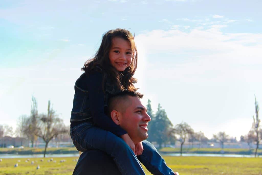 Joel Campos carrying his daughter on his shoulders outdoors in Area 1