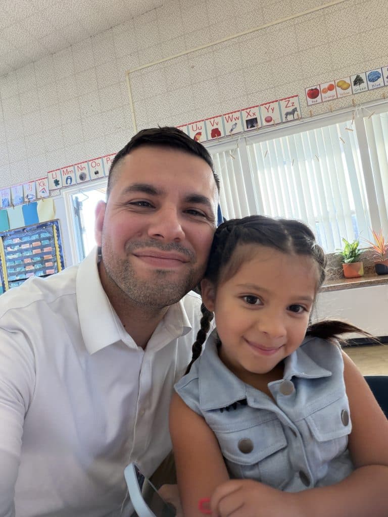 Joel Campos smiling with his daughter in a classroom